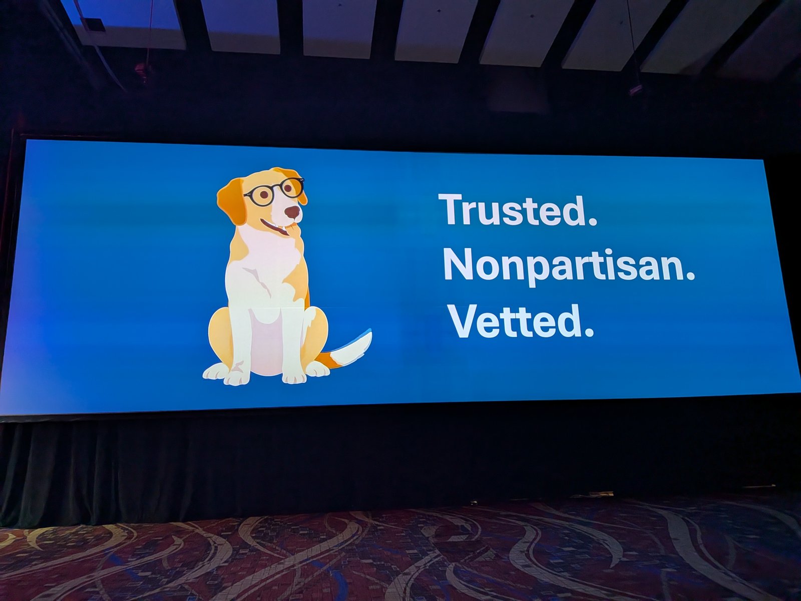 A large ballroom screen showing an illustrated dog with glasses next to the words Trusted, Nonpartisan, Vetted.
